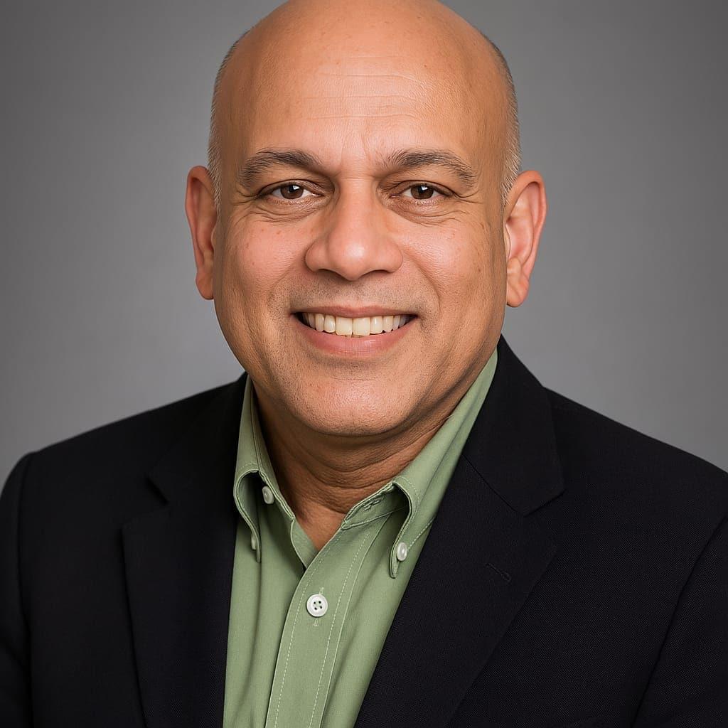 Studio portrait of Paul D'Souza in a dark blazer over a sage shirt