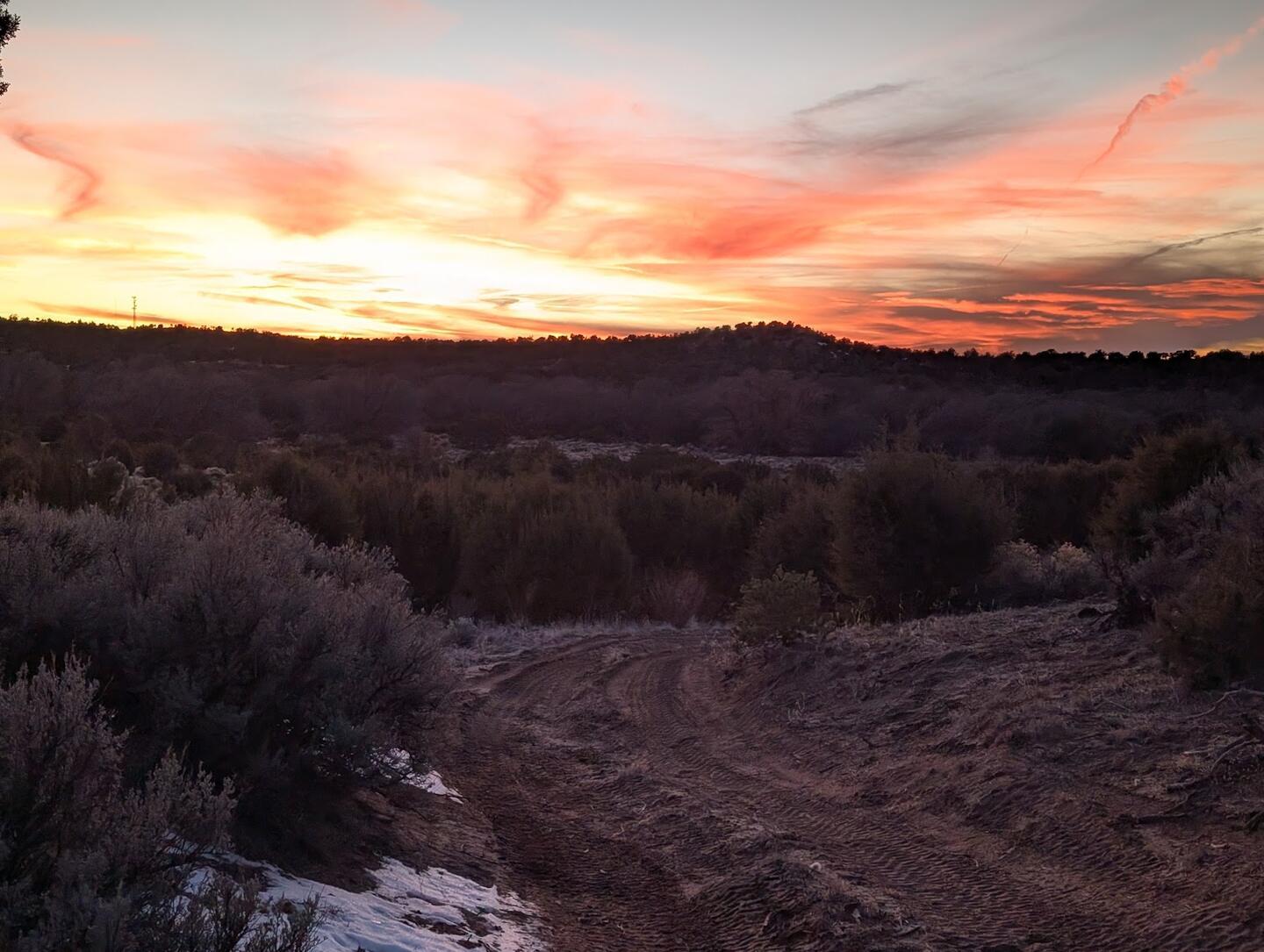 Pink and orange streaks over a dark sagebrush ridge, a dirt track in the foreground