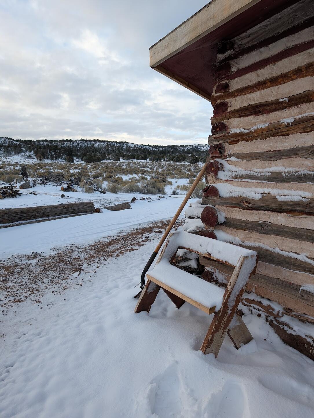 Snow heaped on a wooden bench against the log cabin wall