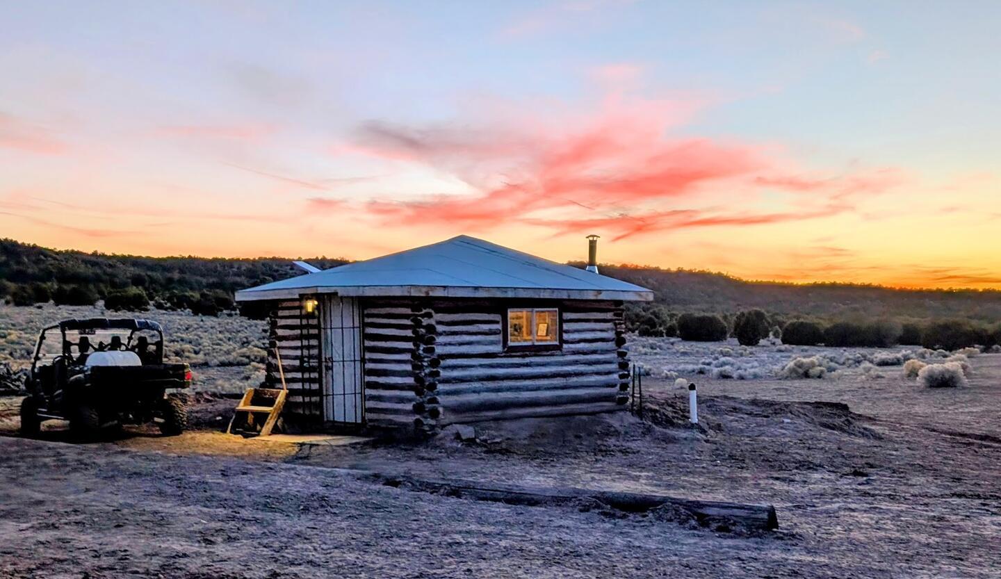 The log cabin at dusk with a utility vehicle parked beside it and pink cloud overhead