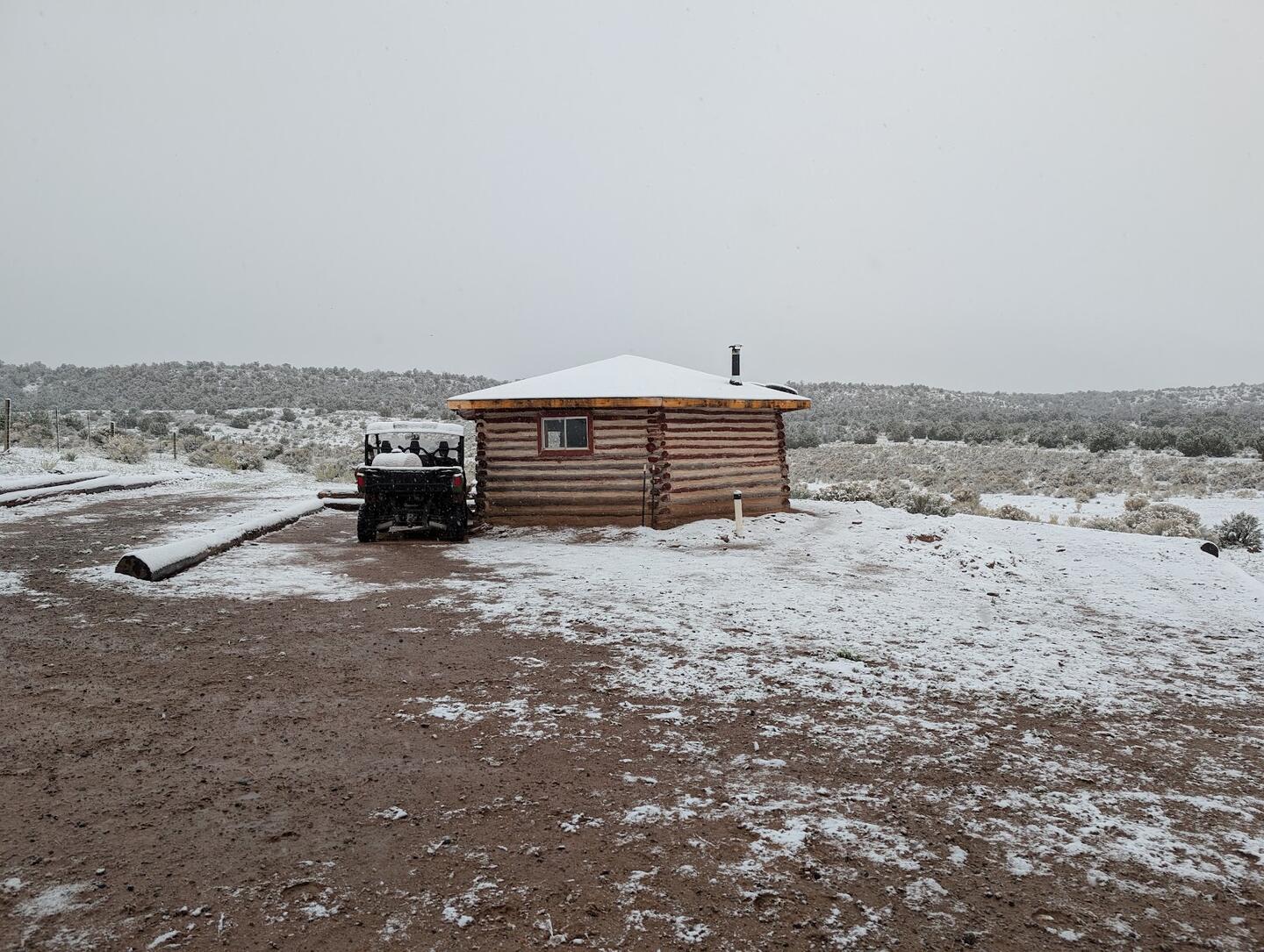 Light snow over the log cabin and a pickup beneath a grey sky