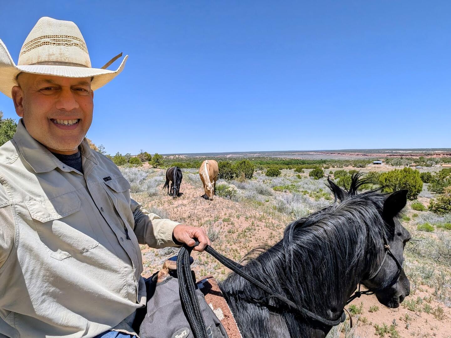 Paul D'Souza on a black horse above the valley, palominos grazing beyond