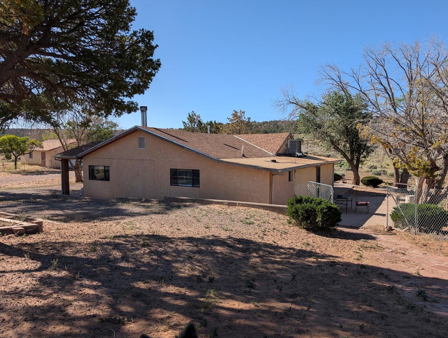 The stucco main house seen from the rise, juniper and cottonwoods around it